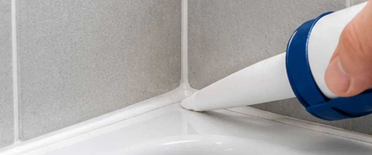 Applying a fresh bead of white sanitary silicone between bath rim and tiled bathroom wall