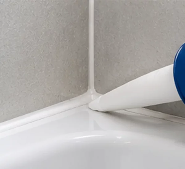 Applying a fresh bead of white sanitary silicone between bath rim and tiled bathroom wall